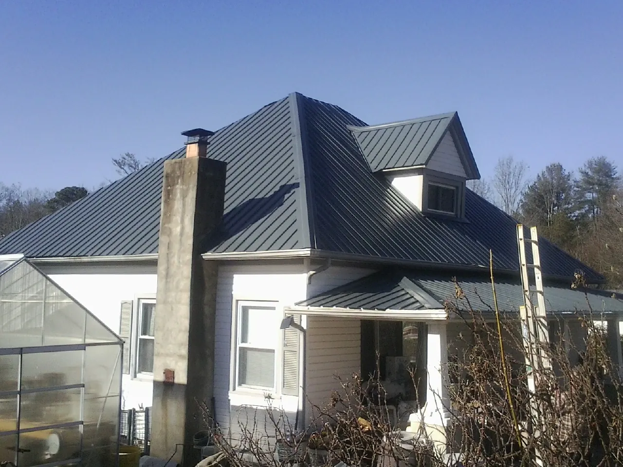 Dark blue standing seam metal roof on a white farmhouse with dormer — Slate & Tile Roof Repair by Roofing Brothers in Wilmot