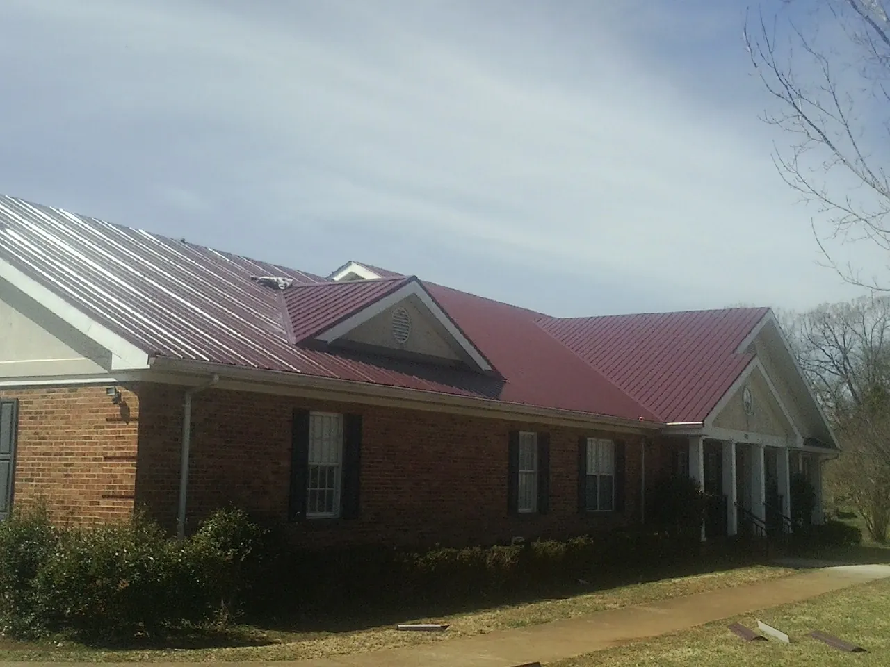 Red metal roof with gabled entries on a long brick building, from a Hail Damage Roof Repair job in Wilmot
