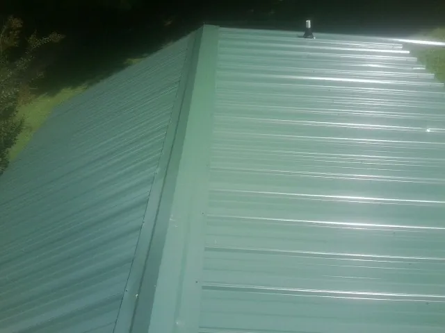New green metal panels meeting at the ridge of a roof — Flat Roof Repair work by our crew in Wilmot