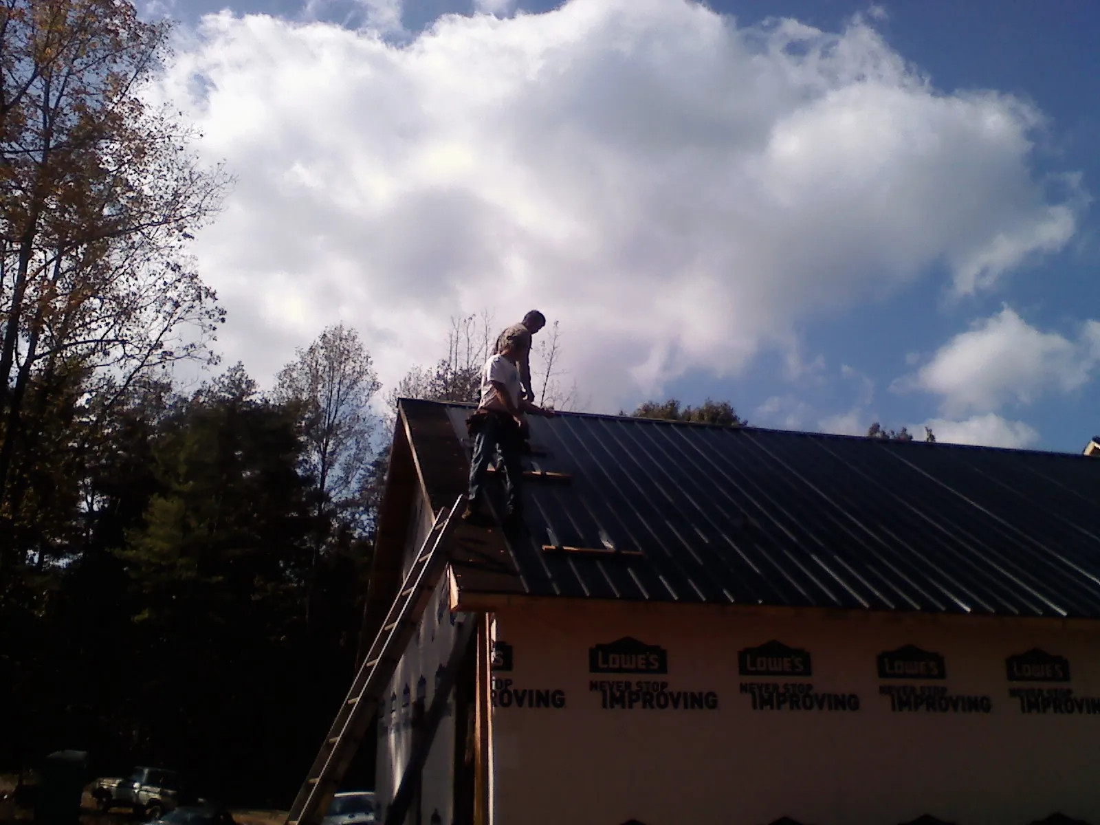 Roofer fastening dark metal panels high against a cloudy sky, from a Roof Inspection job in Wilmot